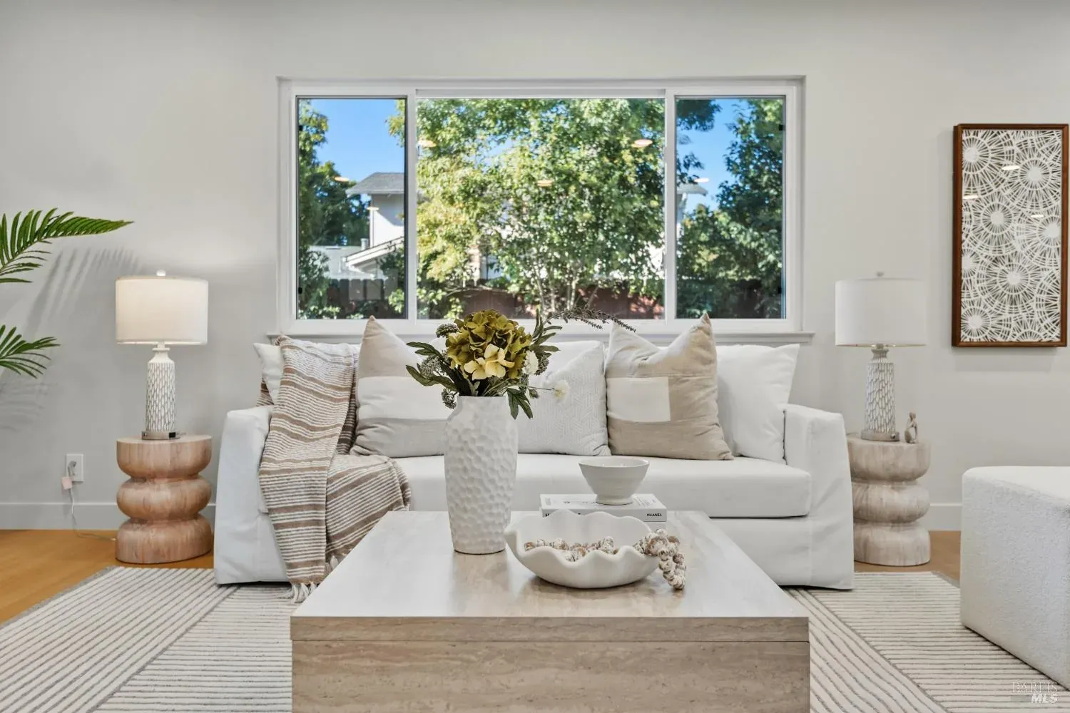 Staged living room with a white slipcovered sofa, travertine coffee table and picture window